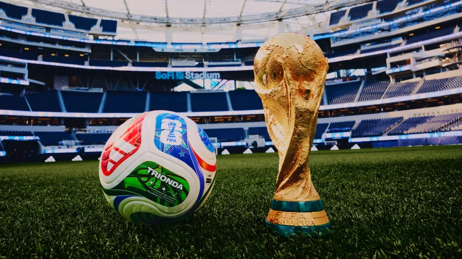 - 香港Gameone娛樂城全新會員福利 - 入金00即返送00! Soccer ball and the FIFA World Cup trophy resting on a grass field inside a large empty stadium.
