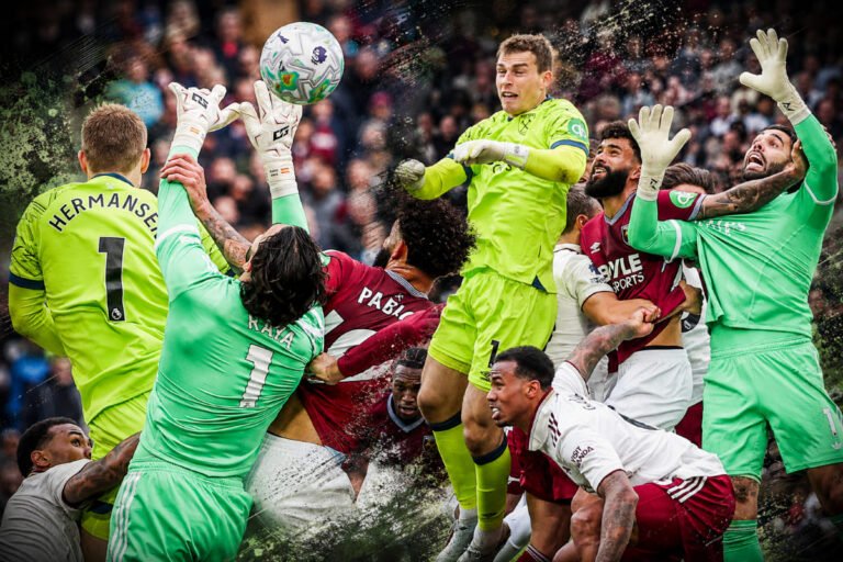 Players clash in a high air for a soccer ball amid a crowded box; lime-green goalkeepers leap with arms raised as maroon-and-white teammates vie for possession